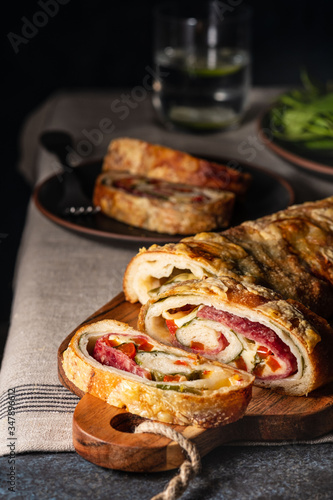 Traditional Italian Stromboli stuffed with cheese, salami, red pepper and spinach. Photo in a dark style.