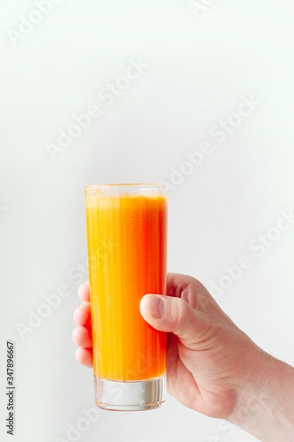 Hand holding glass of carrot juice. Fresh juice on glass isolated on white background.