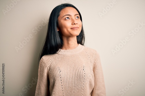 фотографія Young beautiful chinese woman wearing casual sweater over isolated white background smiling looking to the side and staring away thinking