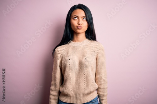 Young beautiful chinese woman wearing casual sweater over isolated pink background making fish face with lips, crazy and comical gesture. Funny expression. © Krakenimages.com