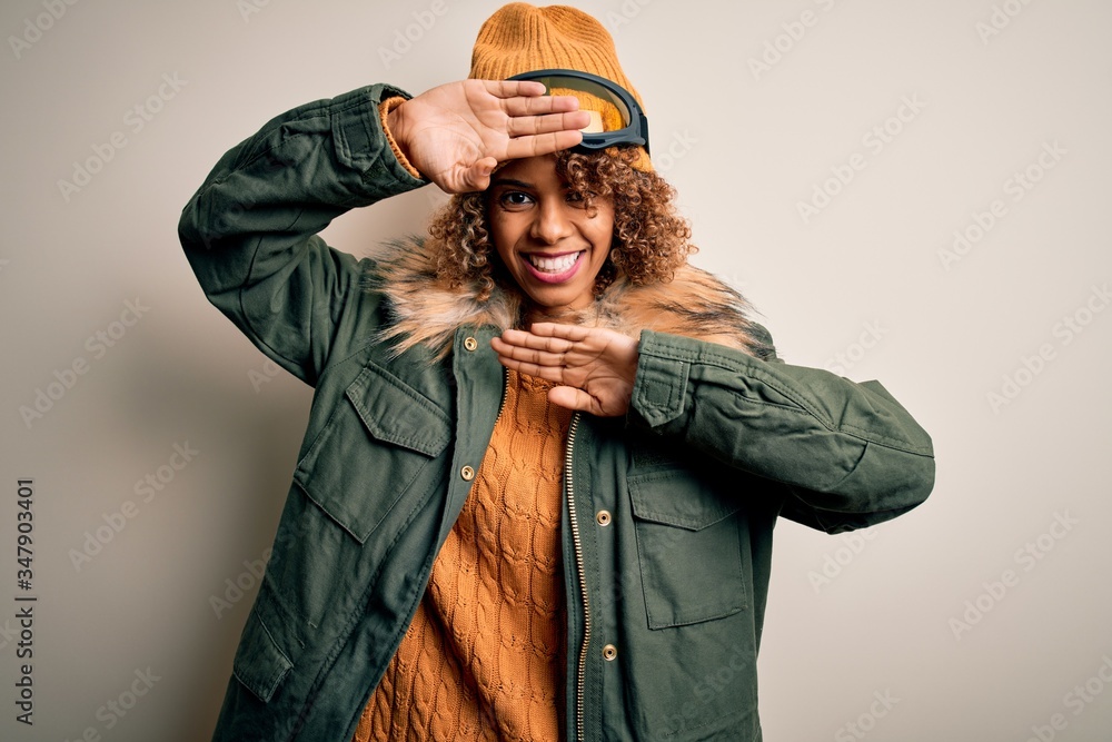 Young african american skier woman with curly hair wearing snow sportswear and ski goggles Smiling cheerful playing peek a boo with hands showing face. Surprised and exited Young african american skier woman with curly hair wearing snow sportswear and ski goggles Smiling cheerful playing peek a boo with hands showing face. Surprised and exited