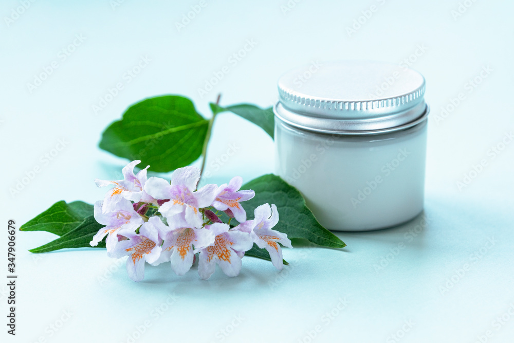 Cosmetic cream in glass jar on white background with flowers. Unbranded package, bio organic natural cosmetics concept