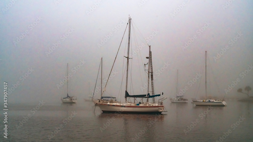 Sailboats anchored in thick grey foggy harbor in the morning Sailboats anchored in thick grey foggy harbor in the morning