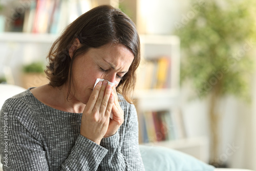 Sick adult woman blowing nose with tissue at home