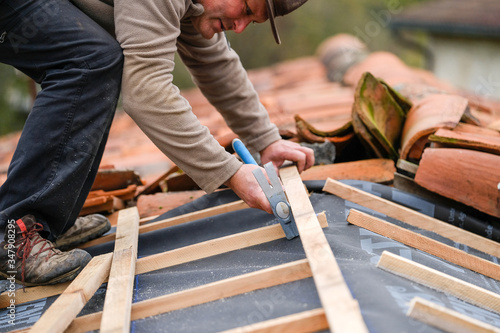 construction worker on a renovation roof covering it with tiles using hammer, crane and grinder