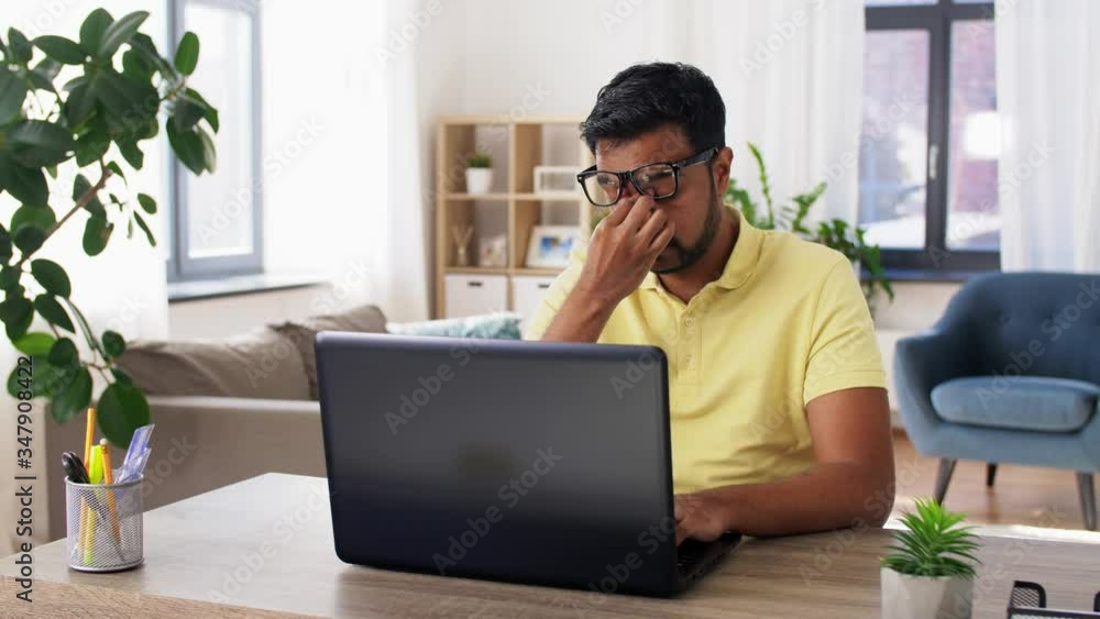 remote job, technology and people concept - tired young indian man in glasses with laptop computer working and rubbing his nose bridge at home office remote job, technology and people concept - tired young indian man in glasses with laptop computer working and rubbing his nose bridge at home office