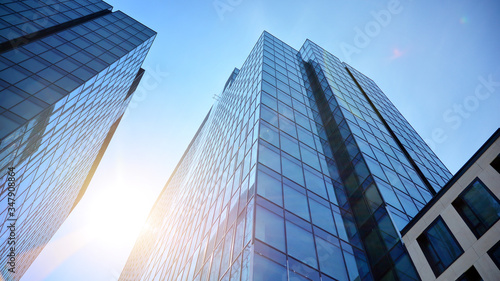 Bottom view of office building window close up with sunrise  reflection and perspective. Modern architecture with sun ray. Glass facade on a bright sunny day with sunbeams on the blue sky. 