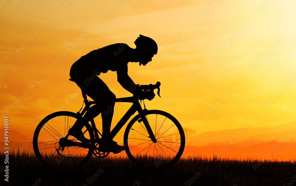 Obraz premium Silhouette of cyclist riding in the field and orange sunset sky.