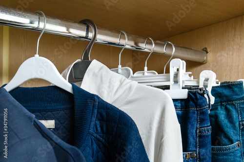 Uniform blue clothes for a teenage boy hanging in a closet on different hangers. There is only one T-shirt in white. The concept is the uniformity of clothes.