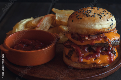 hamburger with french fries, with cheddar cheese, bacon, tomato sauce and mayonnaise on wooden background