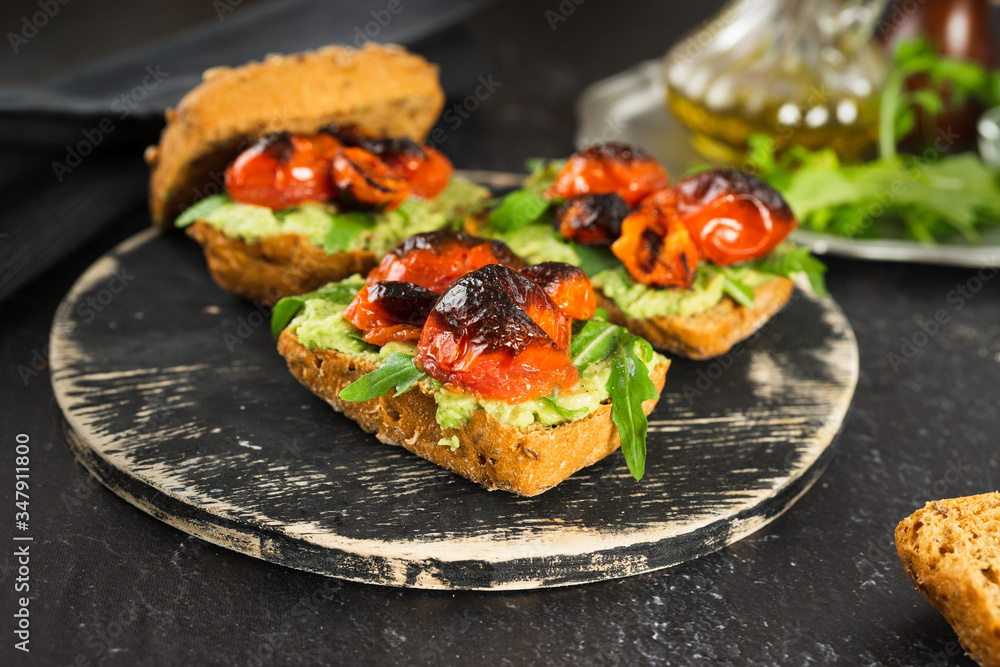 Close up of delicious vegan sandwiches with mashed avocado, roasted tomatoes and arugula Close up of delicious vegan sandwiches with mashed avocado, roasted tomatoes and arugula