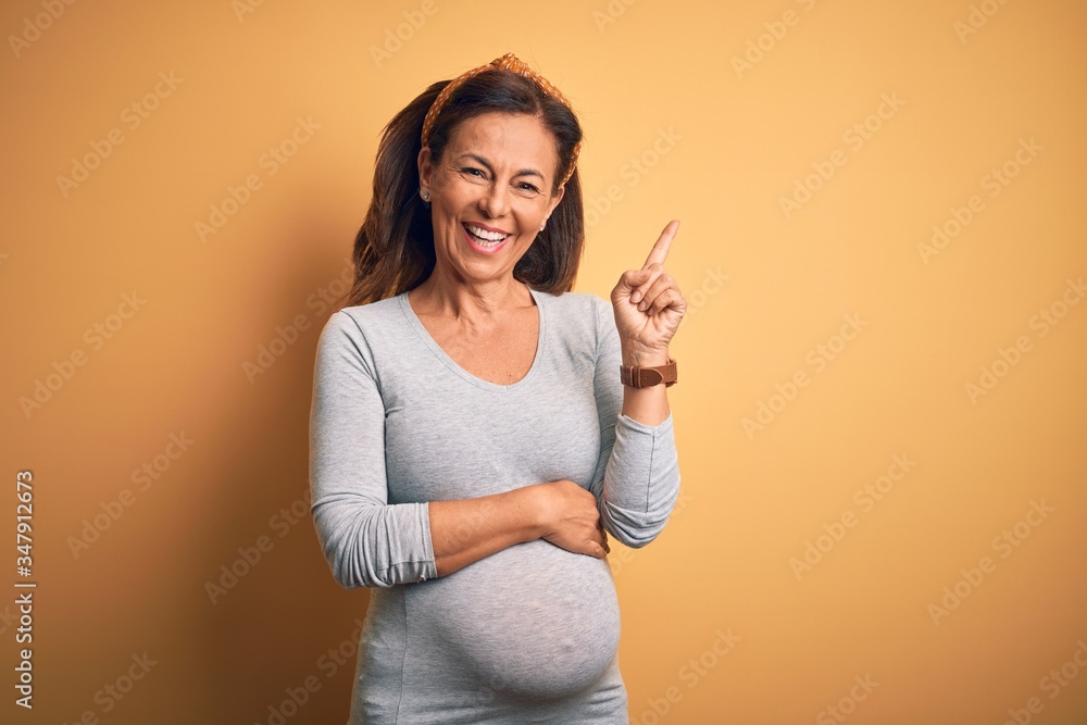 Middle age pregnant woman expecting baby at aged pregnancy with a big smile on face, pointing with hand and finger to the side looking at the camera. Middle age pregnant woman expecting baby at aged pregnancy with a big smile on face, pointing with hand and finger to the side looking at the camera.