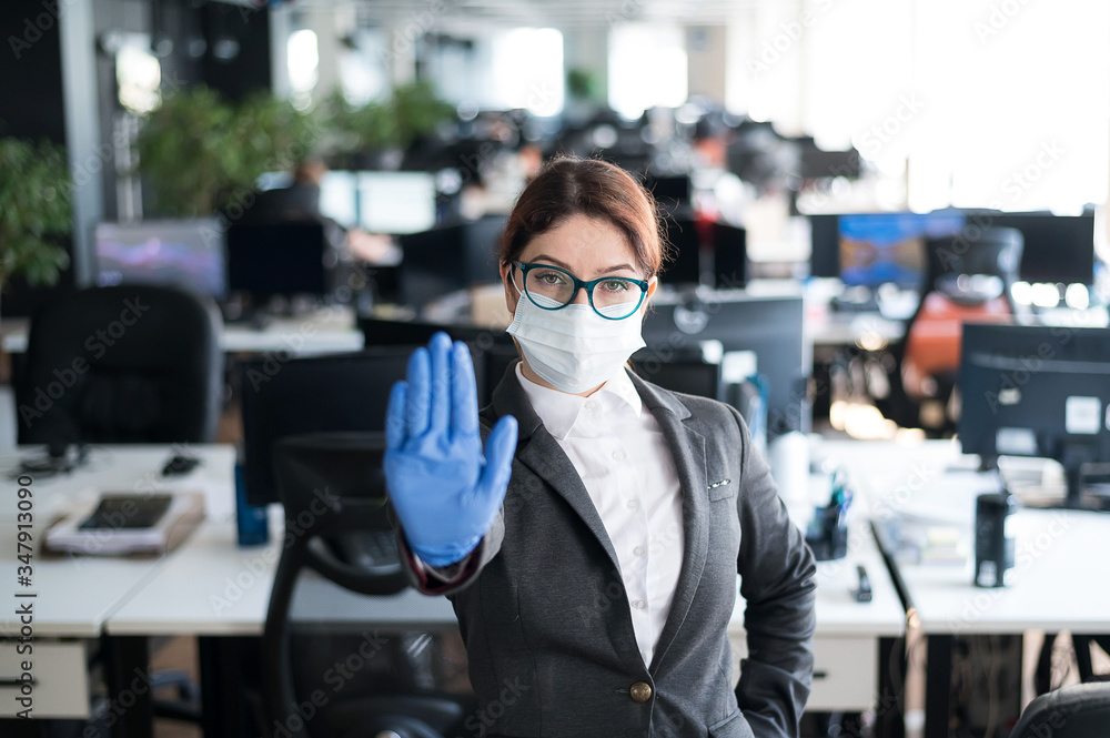 Female office manager in a medical mask and gloves. A woman in a suit uses infection protection. The girl gestures to stop the spread of the coronavirus. Female office manager in a medical mask and gloves. A woman in a suit uses infection protection. The girl gestures to stop the spread of the coronavirus.