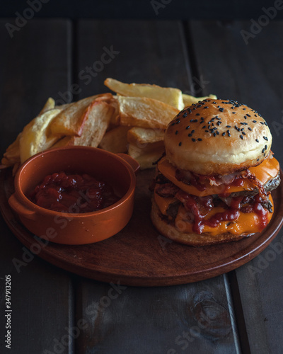 hamburger with french fries, with cheddar cheese, bacon, tomato sauce and mayonnaise on wooden background