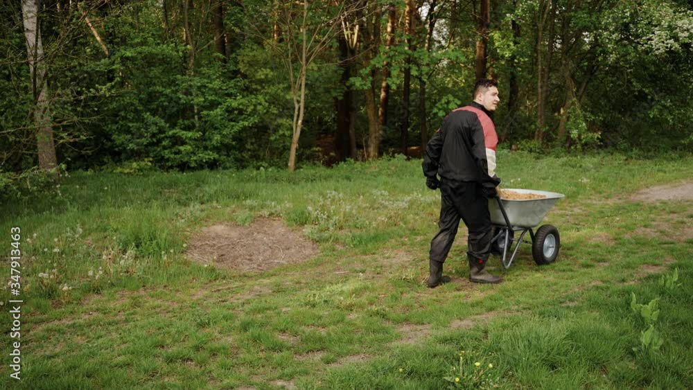 Worker in uniform going with wheelbarrow in the forest with sand. A young man in his prime. Hard work Worker in uniform going with wheelbarrow in the forest with sand. A young man in his prime. Hard work
