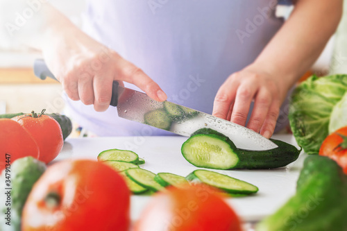 Chef slicing vegetables and cucumber on the table in restaurant. Process of cutting and preparation food in kitchen.