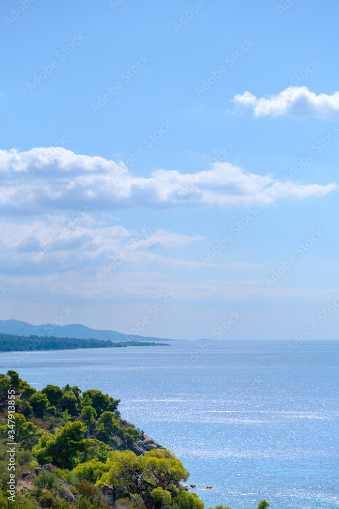 Vertical seascape with blue water , white clouds and green hill