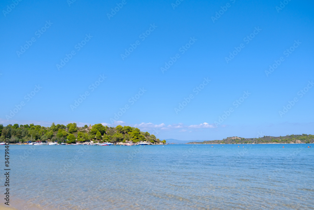 Landscape of turquoise water with green hill in the background and blue sky during summer day
