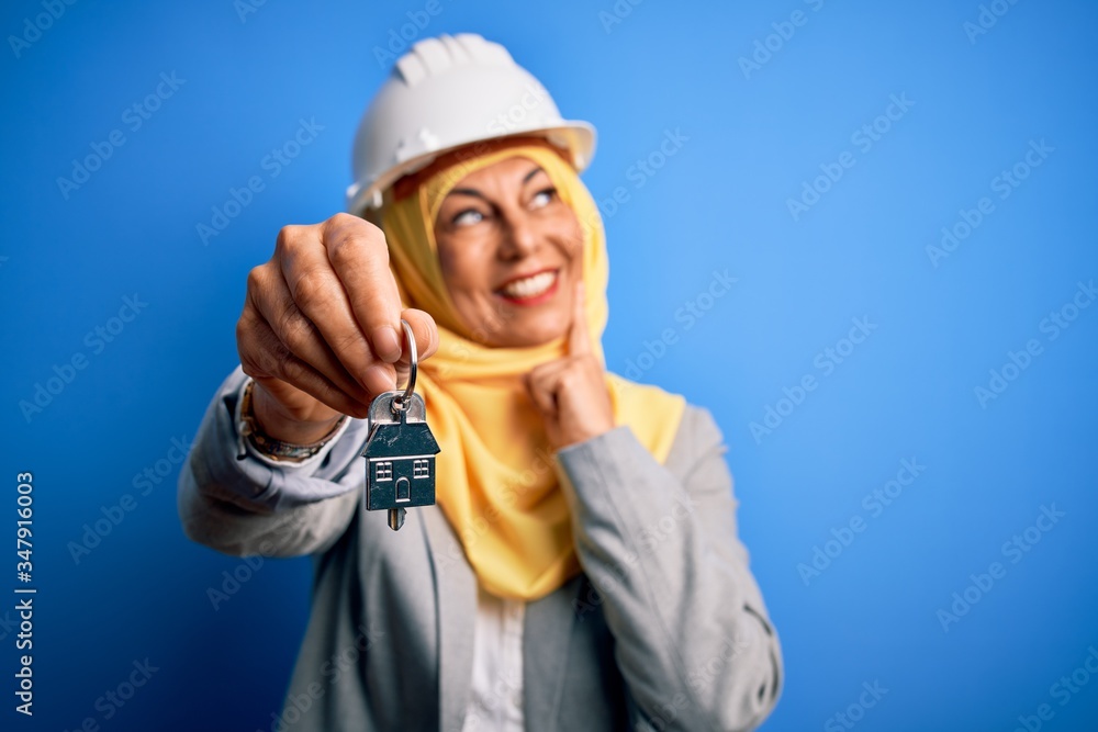 Middle age architect woman wearing muslim hijab and security helmet holding home keys serious face thinking about question, very confused idea Middle age architect woman wearing muslim hijab and security helmet holding home keys serious face thinking about question, very confused idea