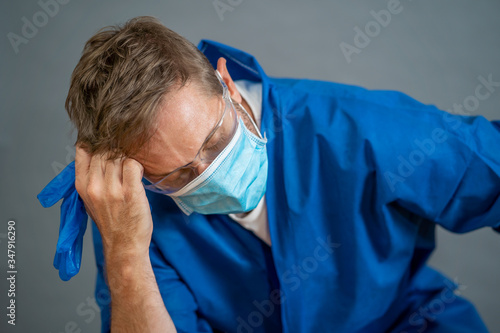 Male doctor feeling exhausted after long shift treating coronavirus infected patients at hospital