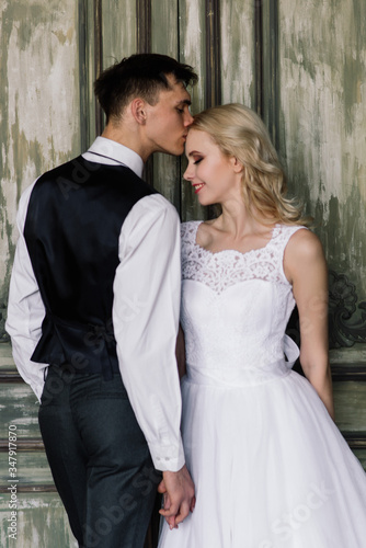 Cute wedding couple in the interior of a classic studio decorated. They kiss and hug each other.