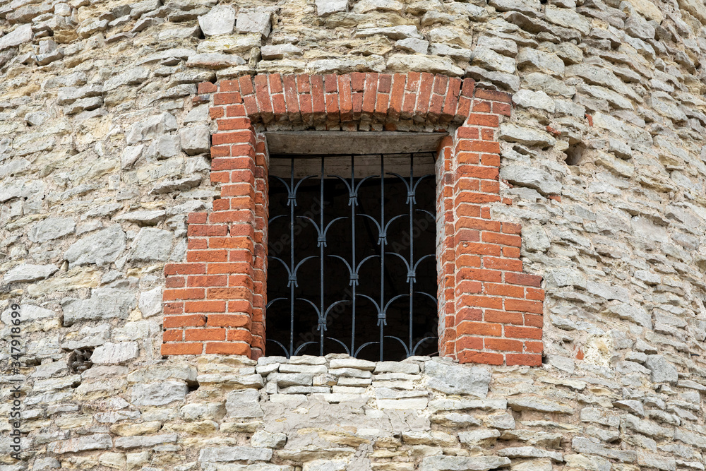 Restored window with wrought-iron bars in the old watchtower of rough stone. Copy space.