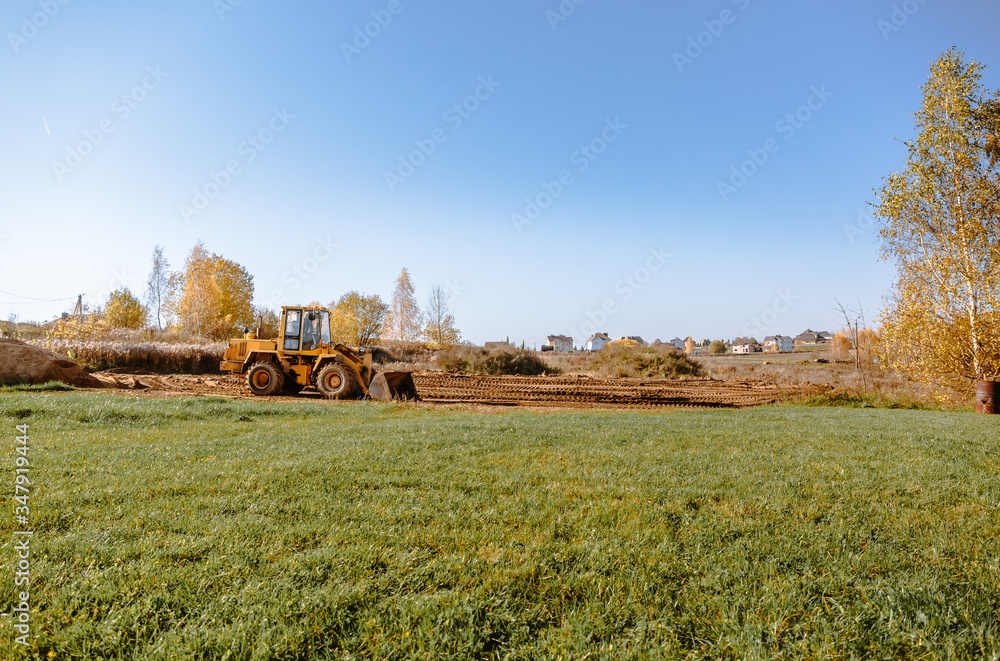 Fototapeta premium large yellow wheel loader aligns a piece of land for a new building. Preparation of the land for the auction. Leveling the landscape and adding sand for construction.
