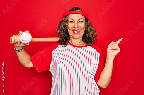 Photography Middle age senior woman wearing baseball equiment, bat and ball over red isolate