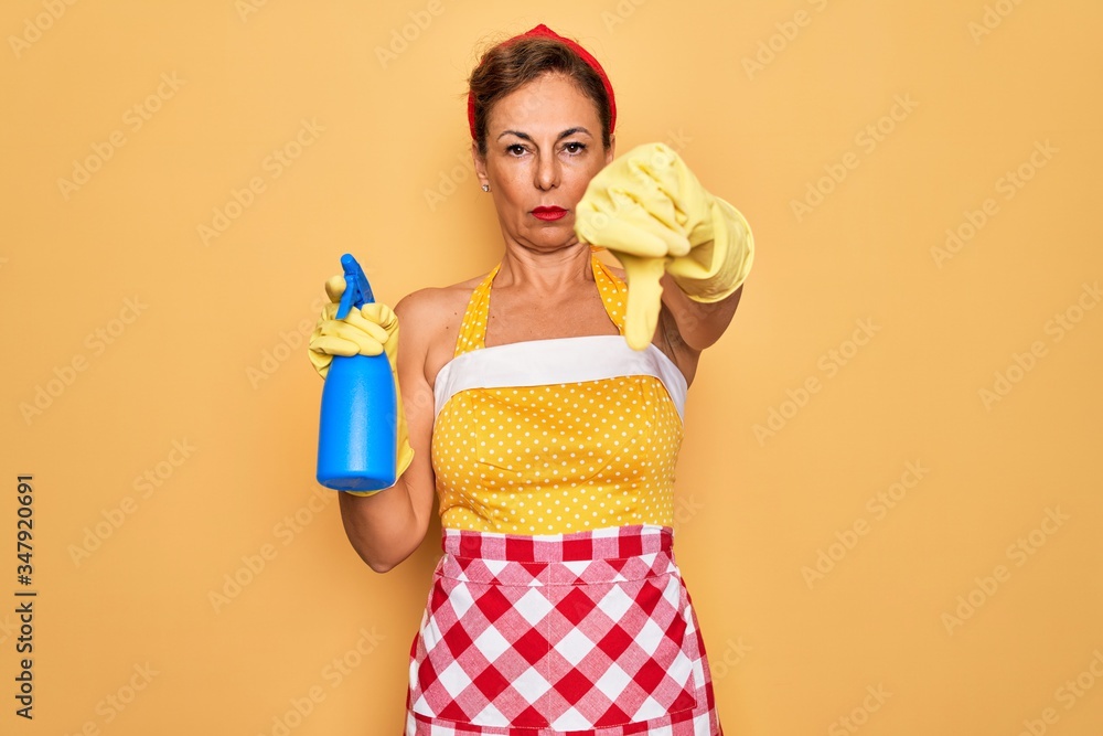 Obraz premium Middle age senior housewife pin up woman wearing 50s style retro dress cleaning using spray with angry face, negative sign showing dislike with thumbs down, rejection concept