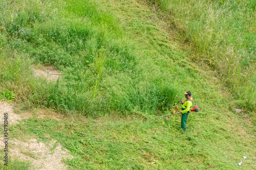 Man in working clothes and equipped with a professional brushcutter cutting the green grass of a solar