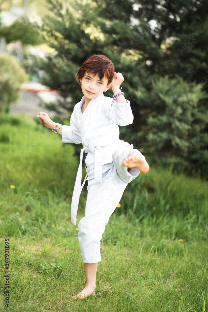 Vertical picture of short haired barefooted 7 years old girl in white kimono making karate training outdoors. Martial arts. Sport and activity for children. Vertical picture of short haired barefooted 7 years old girl in white kimono making karate training outdoors. Martial arts. Sport and activity for children.