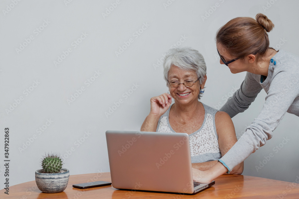 Beautiful mature woman with grey hair using mobile phone while working at home with laptop, wearing eyeglasses messaging with smartphone. Stylish elderly lady browsing site on cellphone, computer. Beautiful mature woman with grey hair using mobile phone while working at home with laptop, wearing eyeglasses messaging with smartphone. Stylish elderly lady browsing site on cellphone, computer.