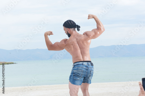 young man on the beach, young muscular man exercising on the beach, young muscular man doing bodibuilding exercises on the beach, athletic young man on the beach