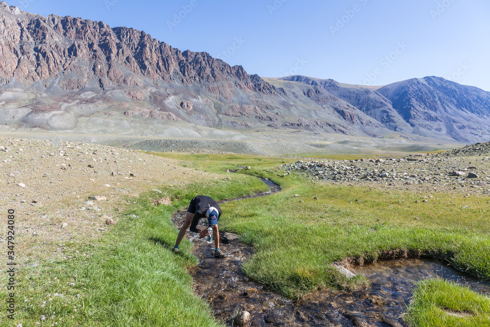 A tourist draws drinking water into a bottle from the mountain river of the Mongolian Altai.