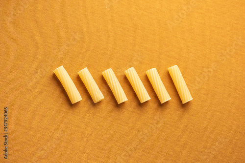 Rigatonis arranged in a row with orange background and soft light
