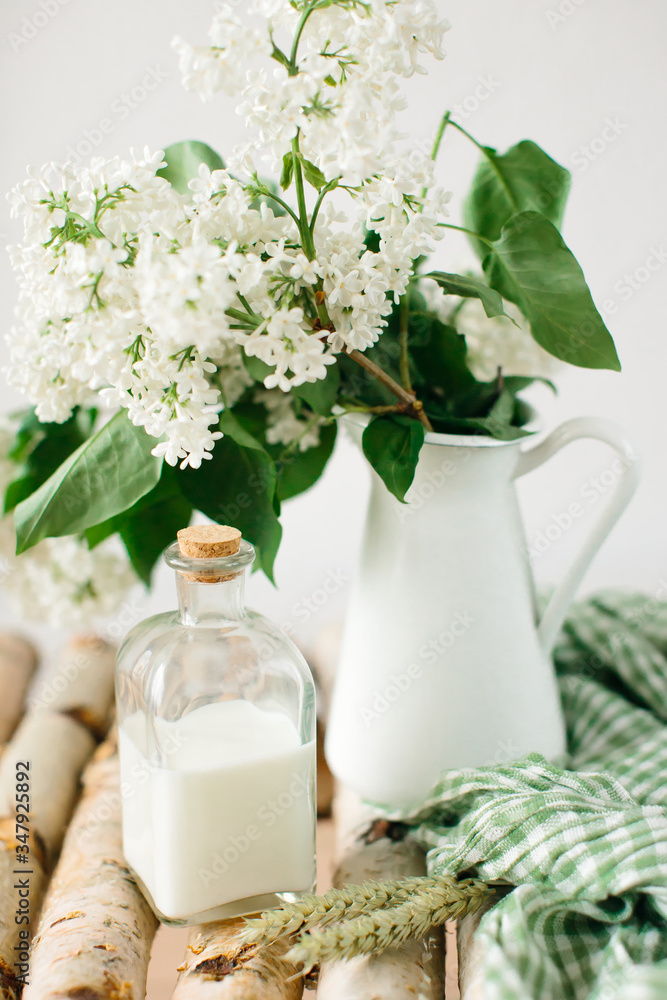 Still life in bright colors, with green accents. Bouquet of white lilac in white vase, next to bottle of milk. Still life in bright colors, with green accents. Bouquet of white lilac in white vase, next to bottle of milk.