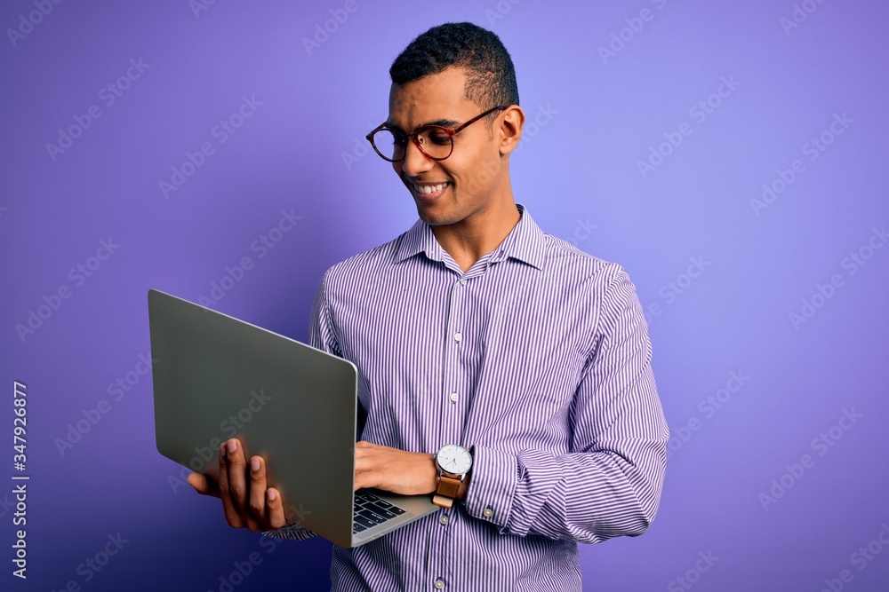 Young handsome african american business man working using laptop over purple background with a happy face standing and smiling with a confident smile showing teeth Young handsome african american business man working using laptop over purple background with a happy face standing and smiling with a confident smile showing teeth