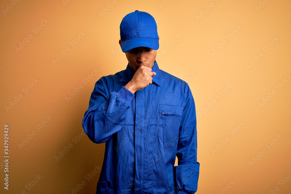 Young african american mechanic man wearing blue uniform and cap over yellow background feeling unwell and coughing as symptom for cold or bronchitis. Health care concept.