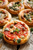 Mini pizza with addition of  tomatoes, capers and green olives sprinkled with fresh herbs on a wooden rustic table, close up