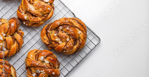 Aerial view of several homemade baked Swedish cinnamon rolls or kanelbulle on a cooling rack. White background with copy space to add text.