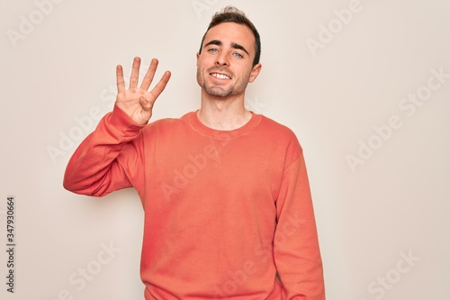 Young handsome man with blue eyes wearing casual sweater standing over white background showing and pointing up with fingers number four while smiling confident and happy. © Krakenimages.com
