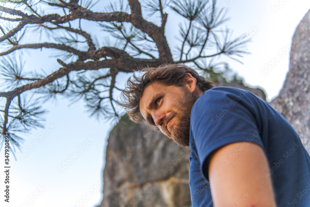 Man in tshirt with beard doing funny face looking down under tree Man in tshirt with beard doing funny face looking down under tree