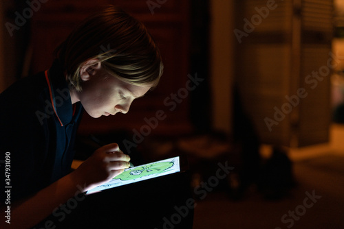 Profile of Tween drawing with stylus on tablet indoors low lit photo