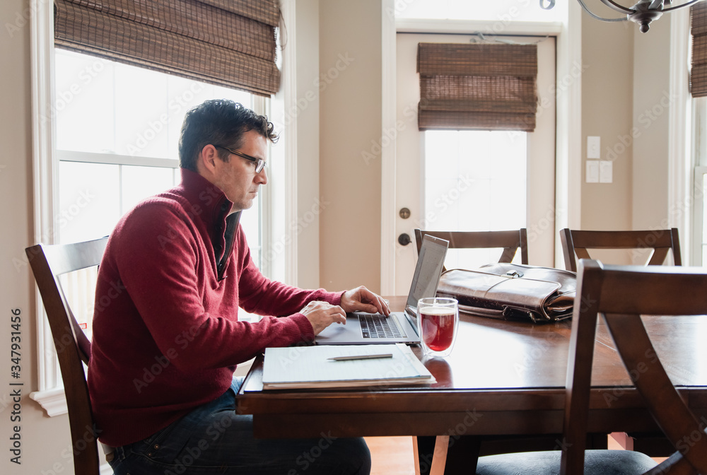Man in glasses working from home using a computer at a dining table. Man in glasses working from home using a computer at a dining table.