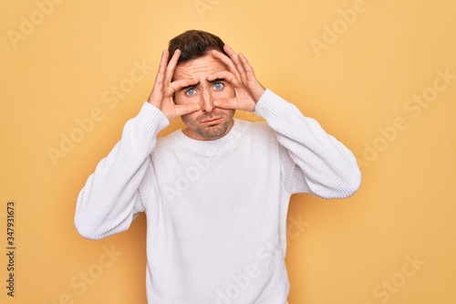 Young handsome man with blue eyes wearing casual sweater standing over yellow background Trying to open eyes with fingers, sleepy and tired for morning fatigue