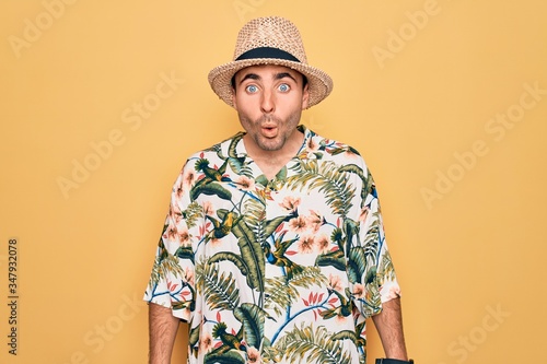 Young handsome man with blue eyes on vacation wearing summer florar shirt and hat afraid and shocked with surprise expression, fear and excited face.
