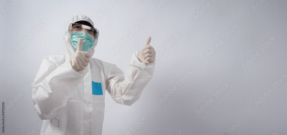 Wide angle images of Asian woman doctor in PPE suit or personal protection equipment and medical goggles, mask, gloves and showing thumb up or like it symbolic which represent happy moment Wide angle images of Asian woman doctor in PPE suit or personal protection equipment and medical goggles, mask, gloves and showing thumb up or like it symbolic which represent happy moment