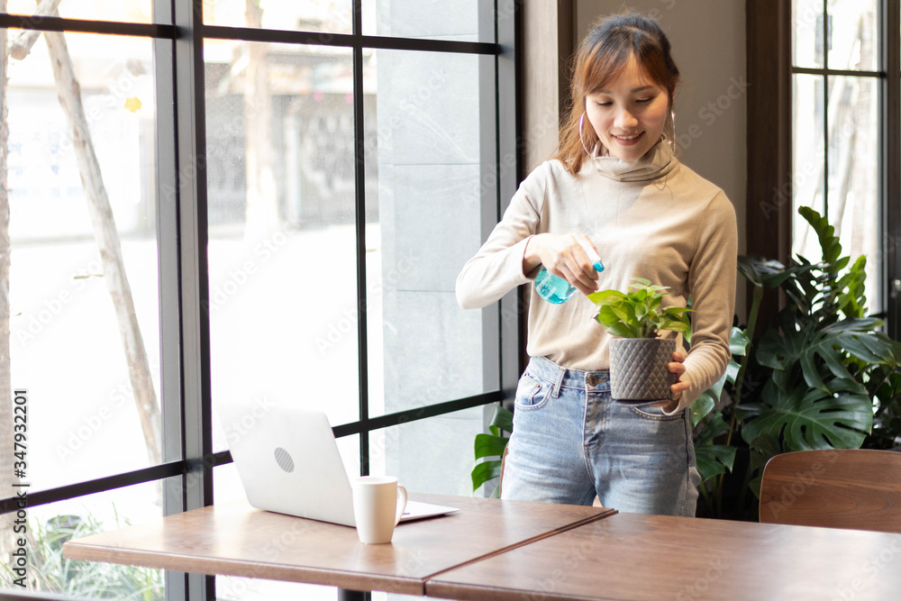Work at home and new normal concept. Young Asian woman water the plant in room. Botanist shop owner happy and smiling while working and success with her business. Work at home and new normal concept. Young Asian woman water the plant in room. Botanist shop owner happy and smiling while working and success with her business.