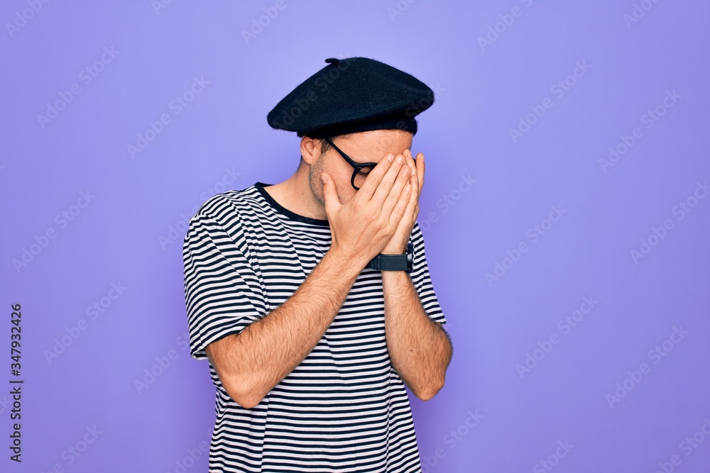 Handsome man with blue eyes wearing striped t-shirt and french beret over purple background with sad expression covering face with hands while crying. Depression concept. Handsome man with blue eyes wearing striped t-shirt and french beret over purple background with sad expression covering face with hands while crying. Depression concept.