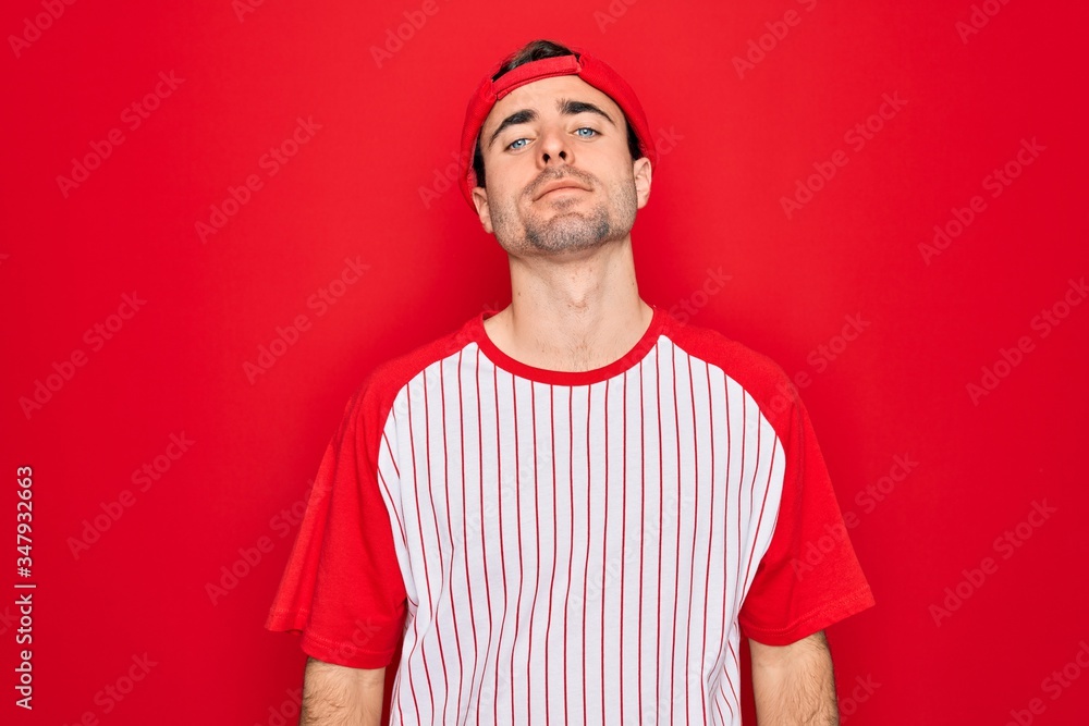 Young handsome sporty man with blue eyes wearing striped baseball t-shirt and cap Relaxed with serious expression on face. Simple and natural looking at the camera. Young handsome sporty man with blue eyes wearing striped baseball t-shirt and cap Relaxed with serious expression on face. Simple and natural looking at the camera.